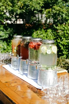 four mason jars filled with water and cucumbers on a wooden table in front of trees