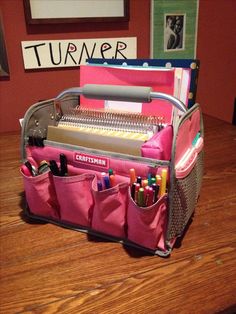 a pink purse filled with school supplies on top of a wooden table next to a wall