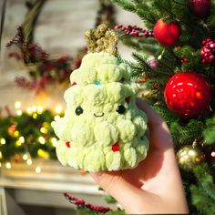 a hand holding up a stuffed animal in front of a christmas tree