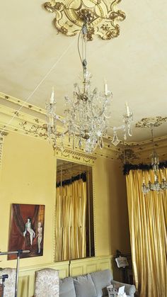 a chandelier hanging from the ceiling in a living room with yellow curtains and gold drapes