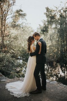 a bride and groom standing together in front of trees