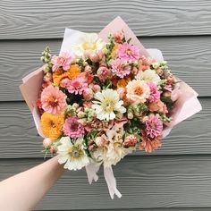 a bouquet of flowers is being held by someone's hand in front of a wooden wall