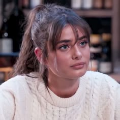 a woman with long hair wearing a white sweater and looking at the camera while sitting down