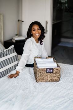 a woman sitting on top of a bed next to a basket filled with folded towels