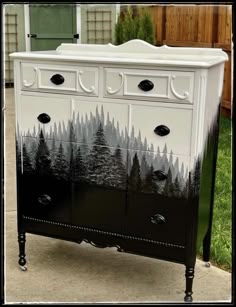 an old dresser has been painted with black and white trees on the front, and is sitting outside