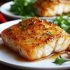 two white plates topped with fish covered in sauce and garnished with parsley