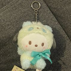 a white stuffed animal with a green bow on it's neck and a tag attached to the key chain