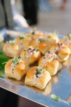 many small rolls with toppings on a metal tray next to some green leafy greens