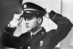 a black and white photo of a man in uniform saluting with his hands on his head