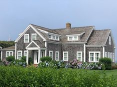 a gray house with white windows and flowers in the front yard on a sunny day