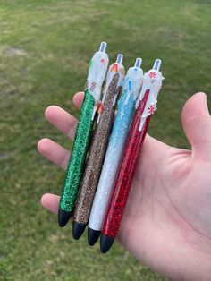 four different colored pens are in the palm of someone's hand, with glitter on them