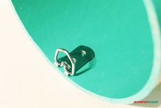 a close up of a metal hook on a green object with a white wall in the background