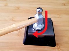 a hammer hitting an object on top of a wooden table with red arrow pointing to it