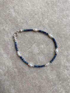 a blue beaded bracelet with white pearls and silver beads on a gray surface,