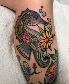 a colorful seahorse tattoo on the leg with flowers and an owl sitting next to it