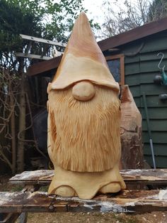 a wooden carving of a gnome with his eyes closed and nose wide open, sitting on a table in front of a house