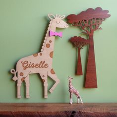 a wooden giraffe standing next to a tree on top of a shelf in front of a green wall