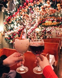 two people toasting wine glasses in front of a christmas tree with ornaments on it