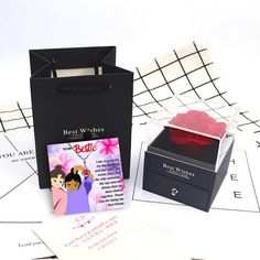 a black box with a red rose in it sitting next to some cards and envelopes