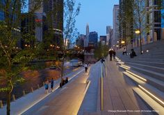 people are walking along the river at night near some tall buildings and trees with lights on them