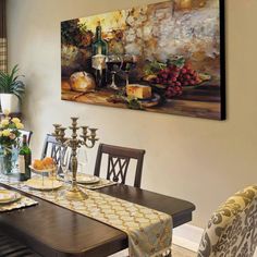 a dining room table set with place settings and wine glasses on it, in front of a painting