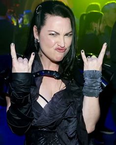 a woman in black dress holding two fingers up to her face and making the peace sign