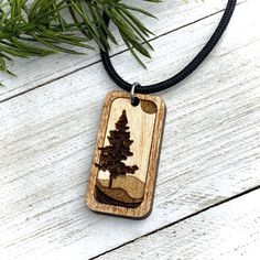 a wooden necklace with a tree in the middle on a black cord hanging from a pine tree