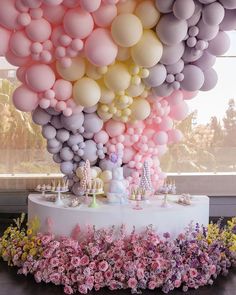 a table topped with lots of balloons and cake next to flowers in front of a window