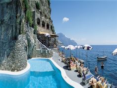 an outdoor swimming pool with chairs and umbrellas next to the cliff side, overlooking the ocean