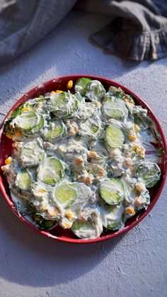 a red bowl filled with cucumbers and cream sauce on top of a table