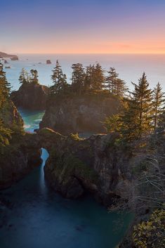 an aerial view of the ocean with trees and cliffs in the foreground, at sunset