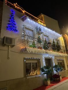 a white building with christmas lights on the balconies and trees lit up at night