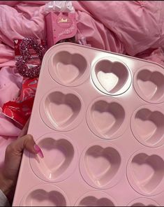 a pink heart shaped muffin pan with lots of hearts in it and someone's hand