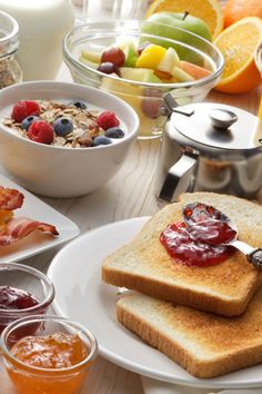 toast, fruit and juice are sitting on the table with other breakfast foods in bowls