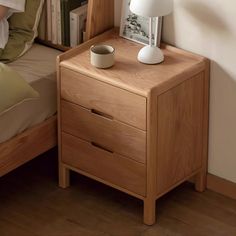 a wooden night stand next to a bed with a white lamp on top of it