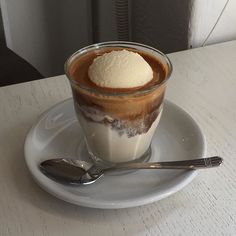 there is a cup of ice cream on the plate with spoons next to it