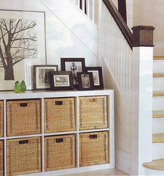 baskets are stacked on top of a white cabinet under the bannister in this entryway