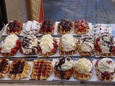 many waffles with different toppings are on display at a street side vendor