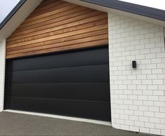 a white brick building with a black garage door and wooden paneling on the side