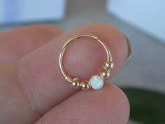 a person is holding a gold nose ring with white opal beads on the end