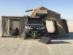 an suv parked in the desert next to a tent and solar panel on top of it