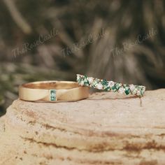 two gold wedding bands with green and white stones on top of a rock in the woods