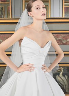 a woman in a white wedding dress with a veil on her head and hands on her hips