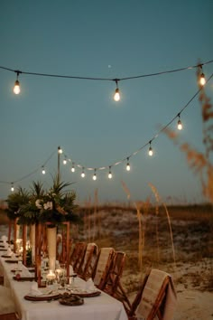 an outdoor dinner table set up with lights strung over it and candles on the tables