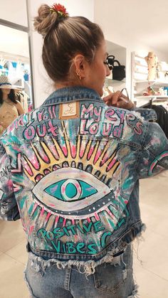 a woman wearing a jean jacket with an eye painted on the front and back side