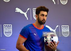 a man holding a soccer ball in front of a purple and blue wall with logos on it