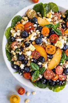 a white bowl filled with blueberries, peaches and spinach on top of a table