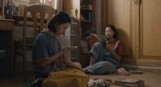 two young women sitting on the floor looking at their cell phones and reading books together