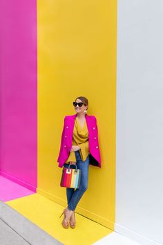 a woman standing in front of a colorful wall with her hand on her hip bag