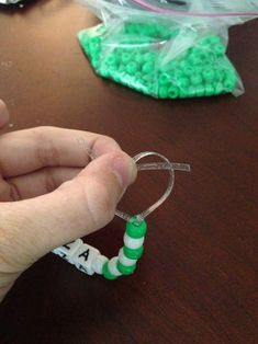 a hand holding a green and white beaded bracelet on top of a wooden table